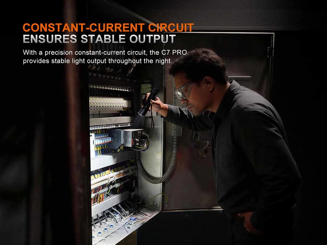 Technician in safety glasses inspecting an open electrical control cabinet with wired circuit boards and components.