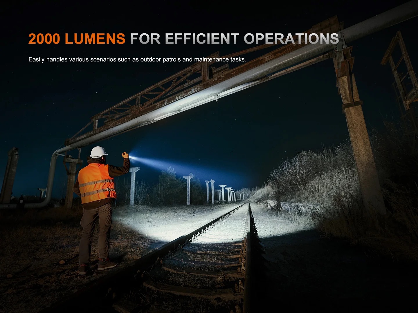 Night scene of a worker in an orange safety vest and white helmet shining a flashlight along rusted railroad tracks at night under industrial structures, promoting bright, efficient lighting.