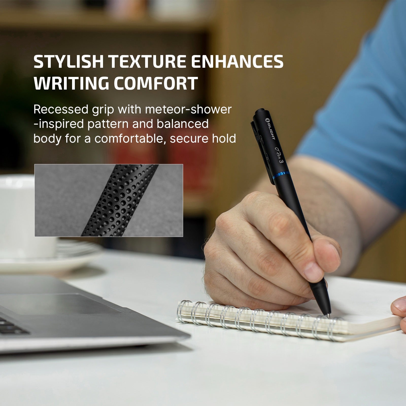 Person writes in a spiral notebook with a black pen on a white desk, with a laptop nearby in the foreground.