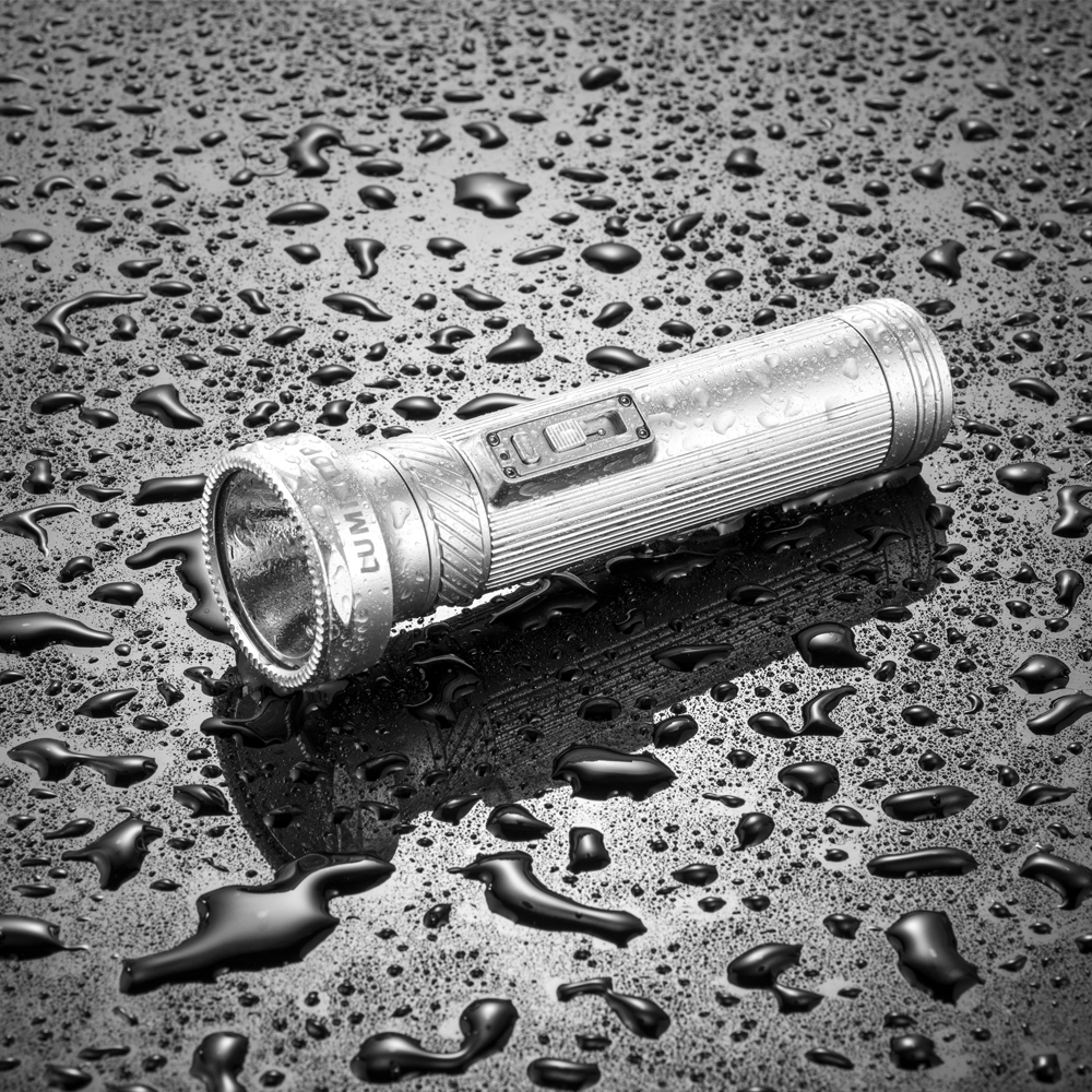 Compact flashlight lying on a wet, reflective surface with scattered water droplets nearby.